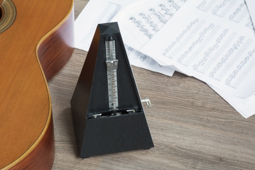 Black metronome with guitar and several notes on the wooden background